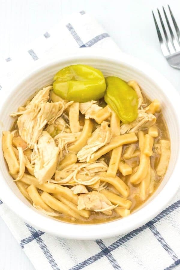 a white bowl filled with Mississippi chicken and noodles that was cooked in the Instant Pot pressure cooker, with pepperoncini as garnish in the bowl