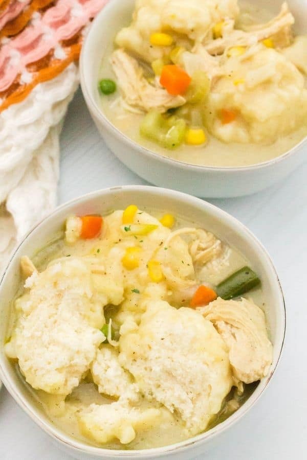 close-up aerial view of two white bowls serving chicken and Jiffy baking mix dumplings, with one dumpling cut in half to show the soft interior