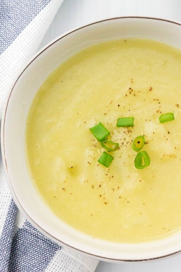 close-up view of a white bowl of Instant Pot potato leek soup topped with sliced green onions
