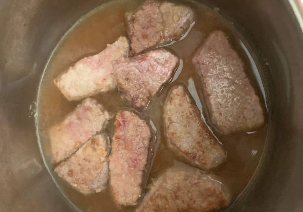 seared beef and broth in the deglazed Instant Pot, prior to adding remaining ingredients for making pressure cooker Swiss steak