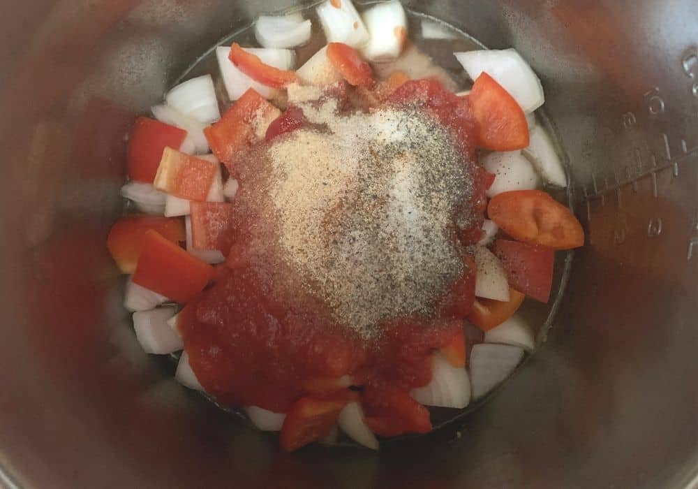 Peppers, onions, tomatoes, and seasonings added to the insert pot of the Instant Pot for the Swiss steak recipe.