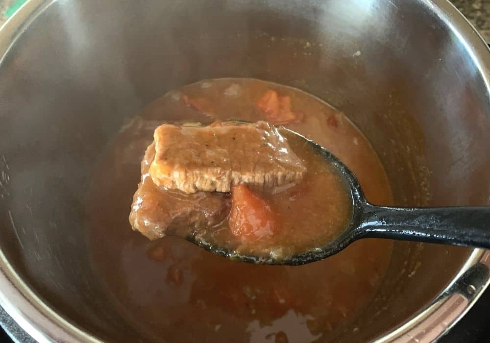 Swiss steak and peppers in thickened tomato gravy being spooned out of the Instant Pot