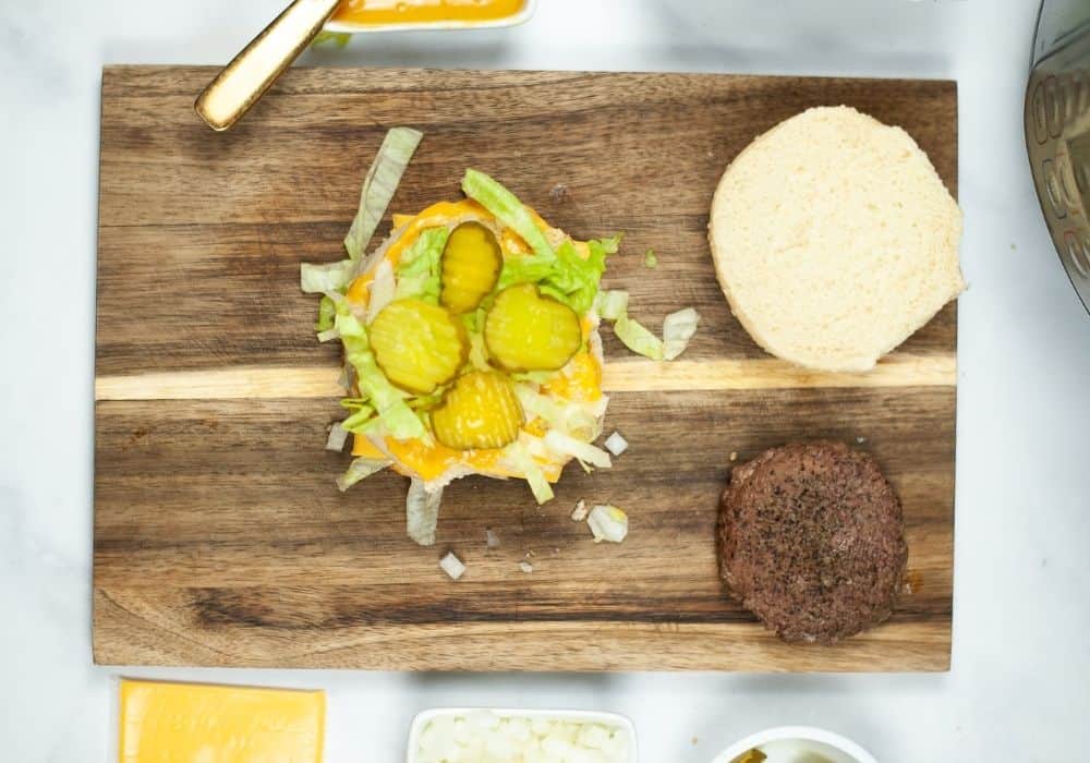 a burger that was cooked in the Instant Pot pressure cooker is being assembled onto a bun with various toppings