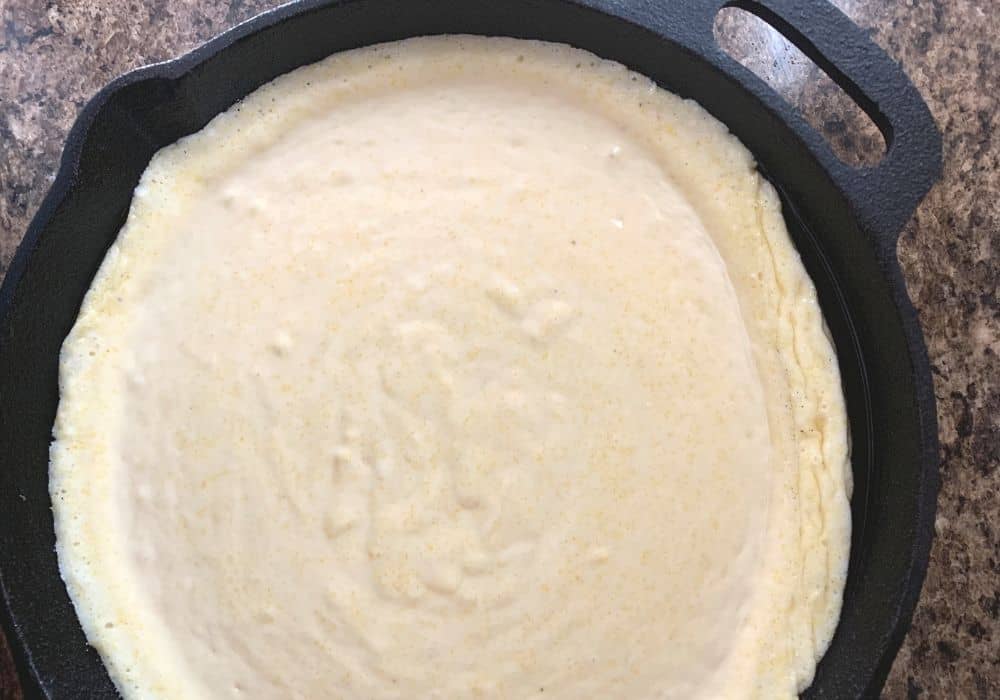 Jiffy cornbread batter in a cast iron skillet, ready to be baked.