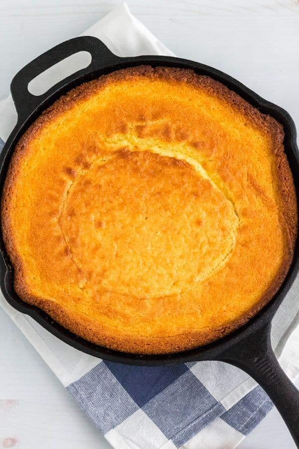 Jiffy cornbread in a cast iron skillet, resting on a blue and white cloth napkin.