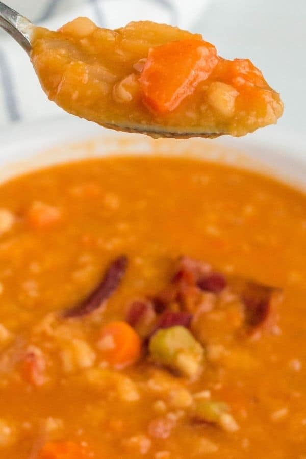 a spoon lifting a scoop of Instant Pot bacon and bean soup from the bowl
