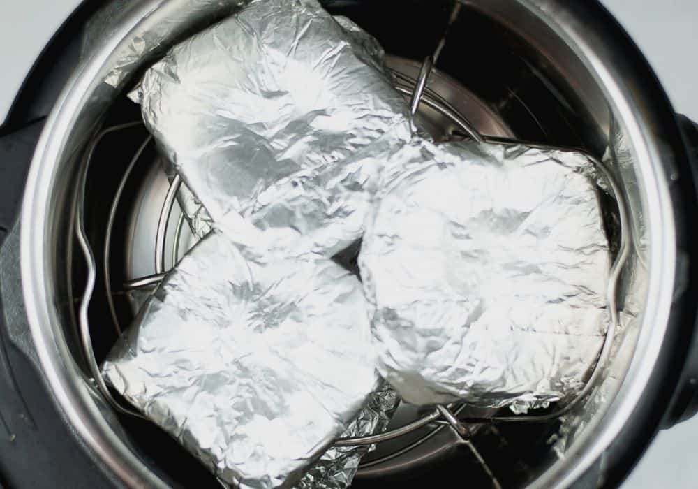 foil-wrapped burgers on top of the trivet in the Instant Pot