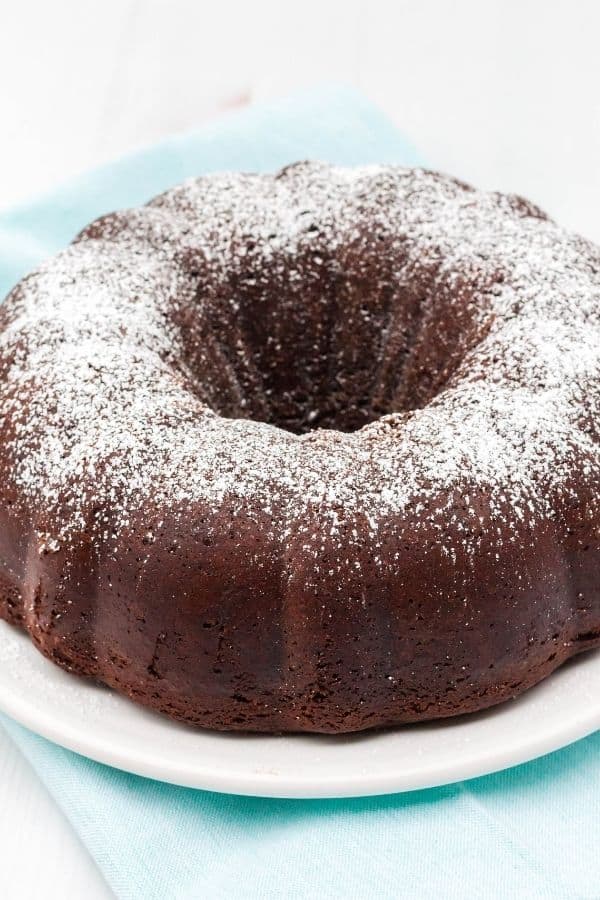 Whole chocolate bundt cake dusted with powdered sugar, served on a white plate.