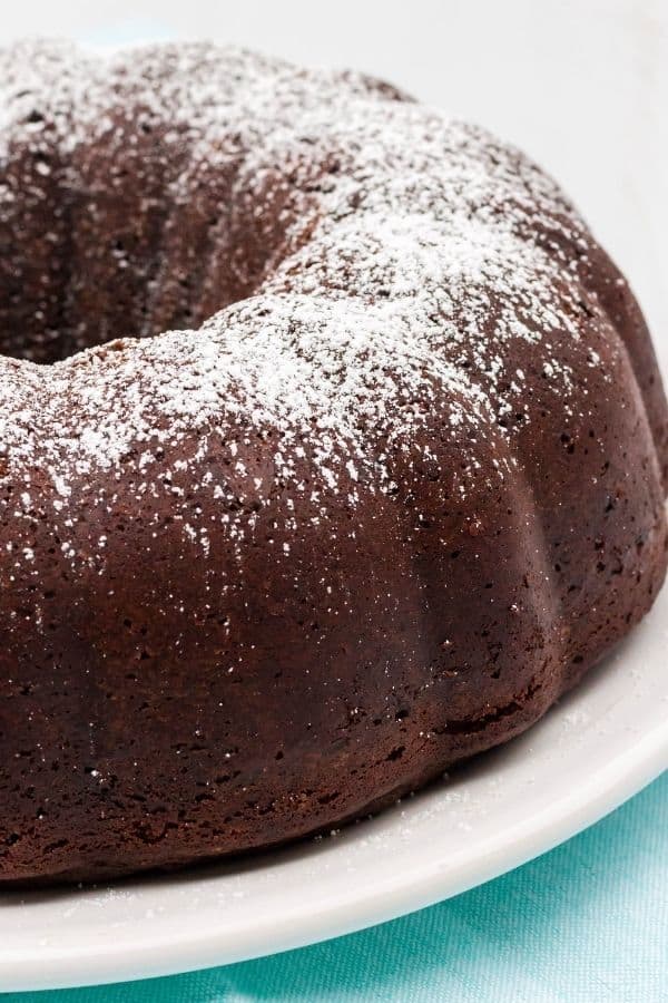 close-up view of the side of an entire chocolate sour cream bundt cake, served on a white platter.