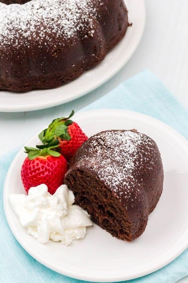 Slice of chocolate sour cream bundt cake served on a white plate with strawberries and cream.