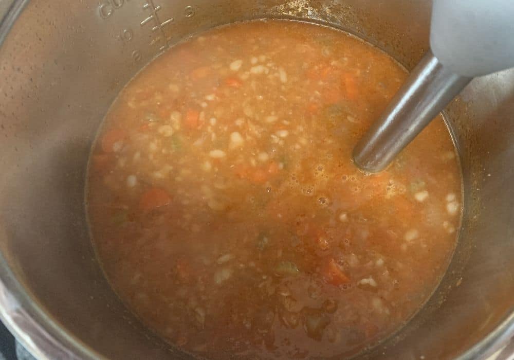 Immersion blender being used to partially puree the bean and bacon soup.