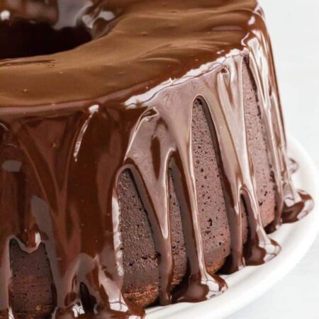 chocolate pound cake made with sour cream, topped with chocolate ganache and served on a white plate