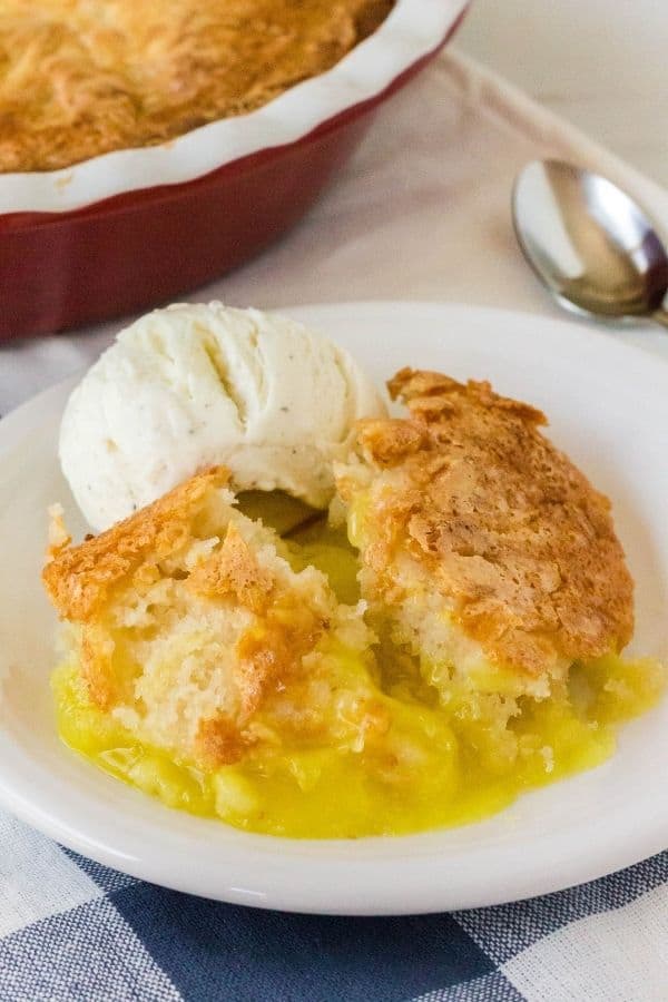 lemon cobbler on a white plate with a scoop of vanilla ice cream, atop a blue and white checked napkin