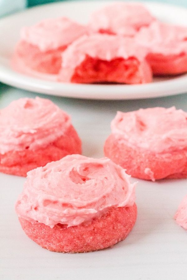 pink strawberry Jello sugar cookies in the foreground, with a few on a plate in the background