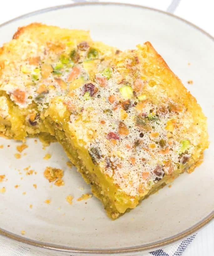 two pistachio lemon bars on a cream-colored plate