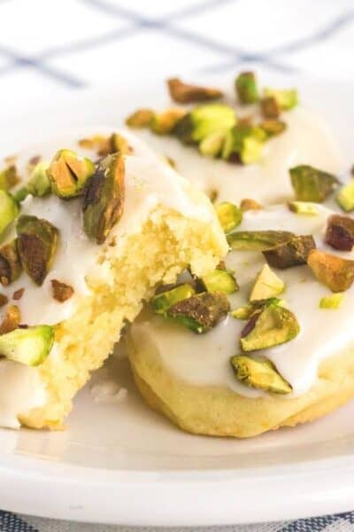 a few lemon pistachio cookies on a white plate, with a bite taken out of one.