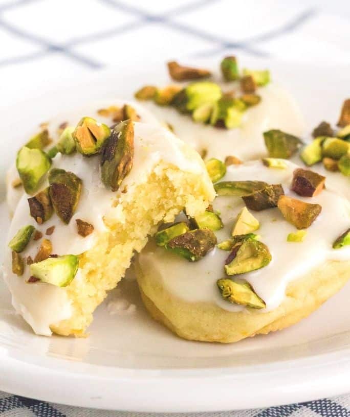 a few lemon pistachio cookies on a white plate, with a bite taken out of one.