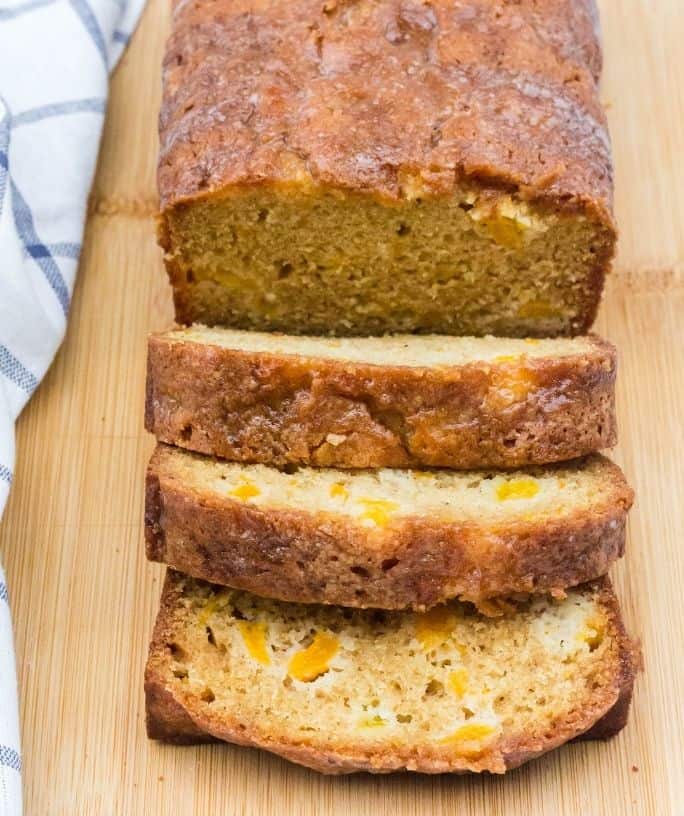 a partially sliced loaf of peach bread on a wooden cutting board