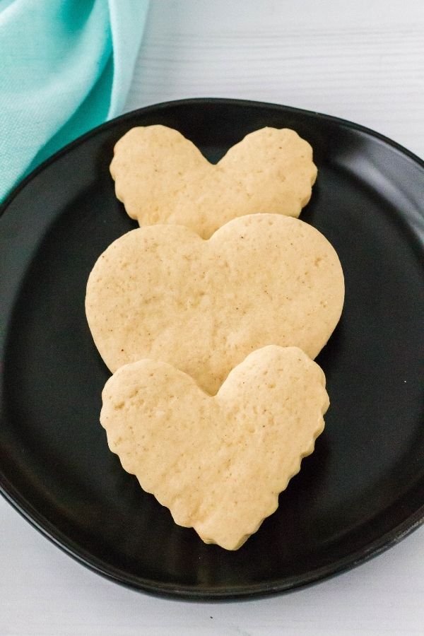 three heart-shaped sour cream cookie cutouts on a black plate