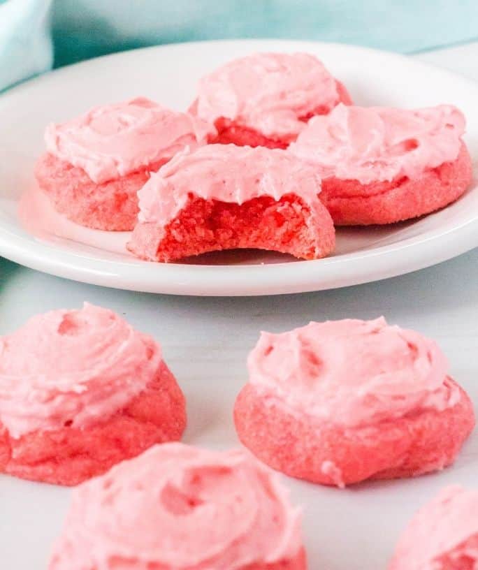 four strawberry jello sugar cookies on a white plate in the background and three cookies in the foreground