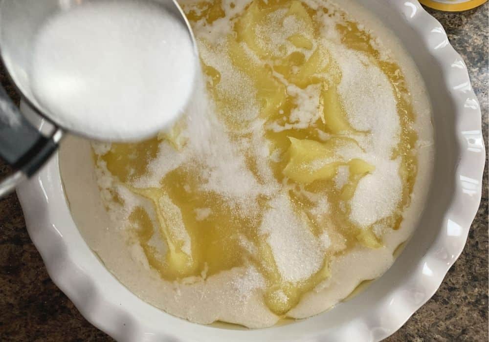 sugar being sprinkled over the lemon cobbler ingredients prior to baking