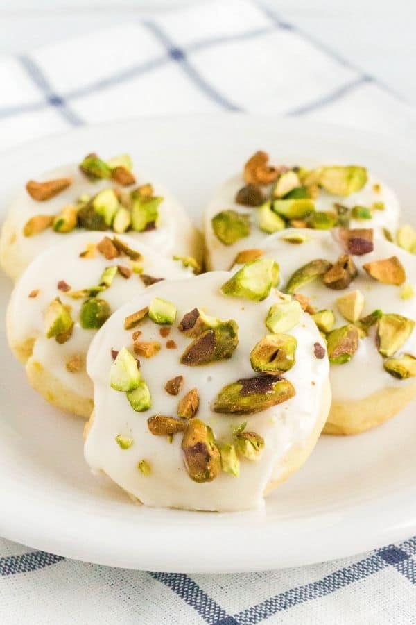 5 lemon pistachio cookies on a white serving plate atop a blue and white checked napkin