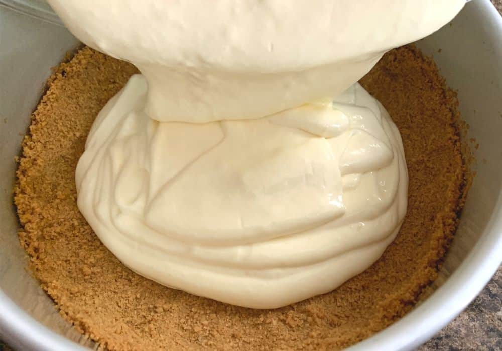 lemon cheesecake batter being poured into prepared crust