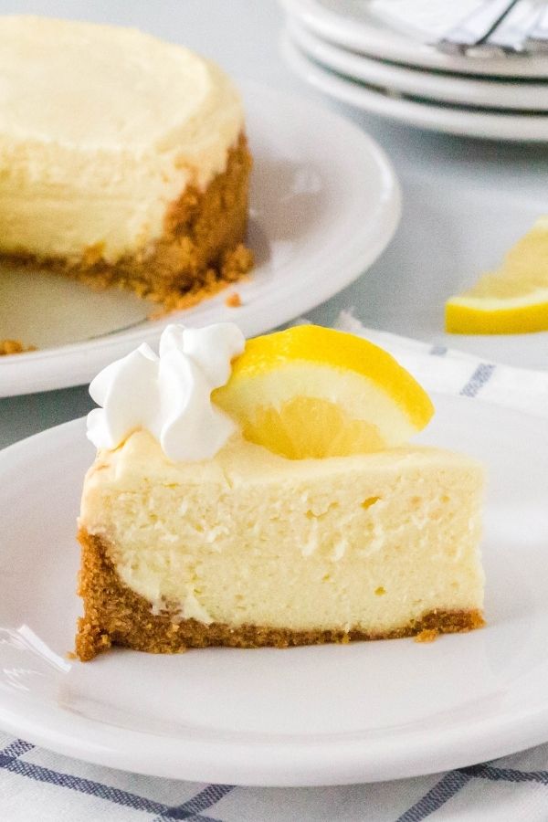 slice of lemon cheesecake that was cooked in the Instant Pot, served on a white plate with whipped cream and sliced lemon