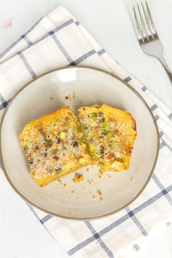 two lemon pistachio bars on a plate, with a fork next to it.