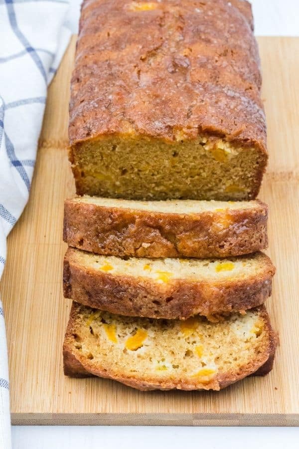 a partially sliced loaf of peach bread on a wooden cutting board