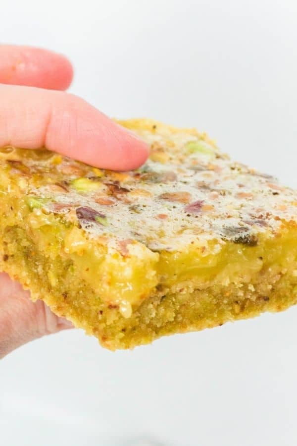 a woman's fingers holding a lemon pistachio bar.