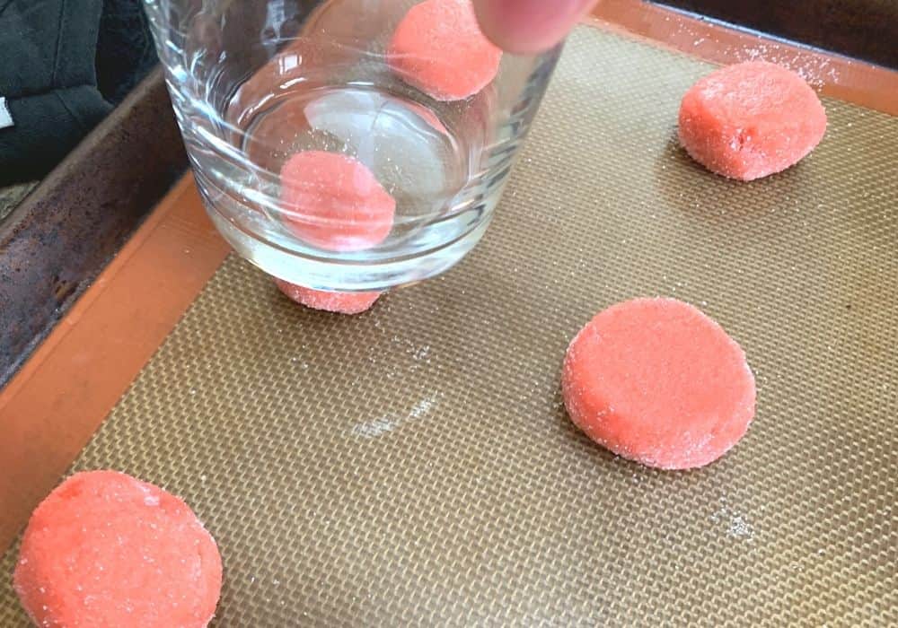 drinking glass being used to slightly flatten the tops of the strawberry sugar cookie dough balls.