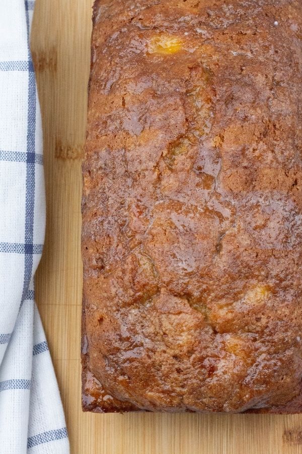 fresh peach bread with a glaze drizzled over the top, served on a wooden cutting board