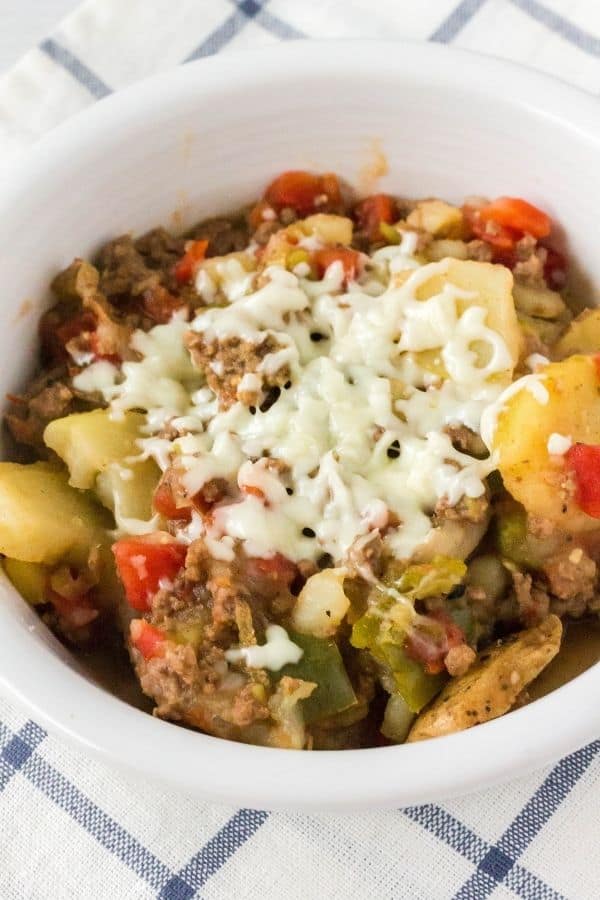 Pressure cooker potatoes, ground beef, peppers, and onions topped with cheese in a white bowl