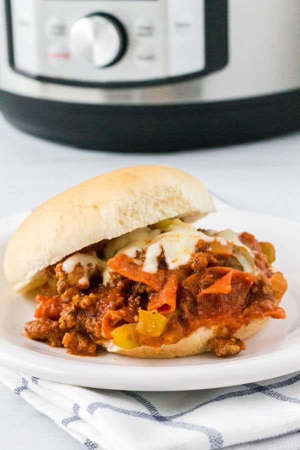 a pizza burger sandwich on a white plate in front of an instant pot pressure cooker