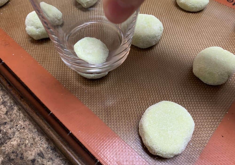 balls of lime jello cookie dough rolled in sugar and being flattened slightly with the bottom of a drinking glass