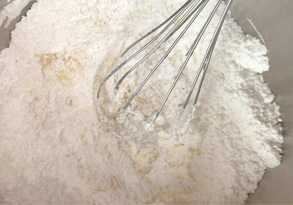 ingredients for vanilla icing being whisked together in a stainless steel bowl