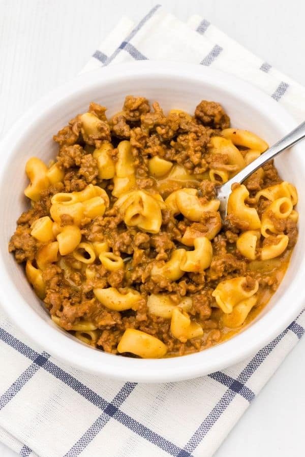 boxed Hamburger Helper cheeseburger macaroni cooked in the Instant Pot is served in a white bowl with a fork.
