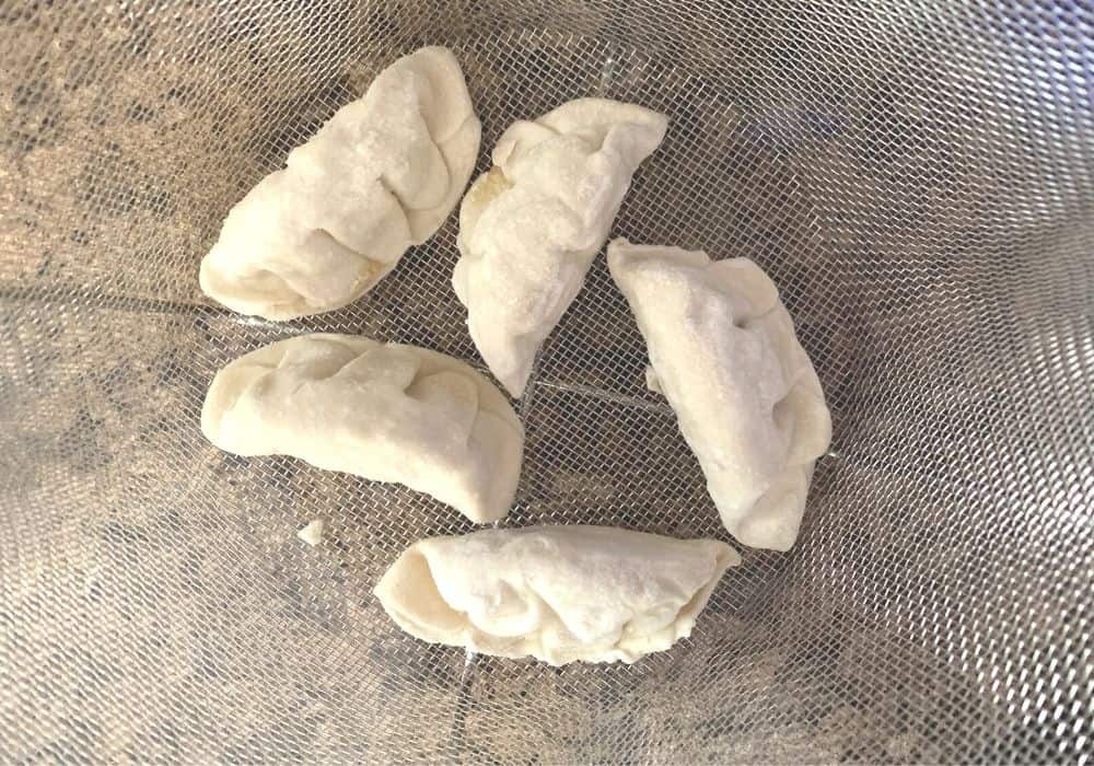 Five frozen dumplings in a steamer basket.