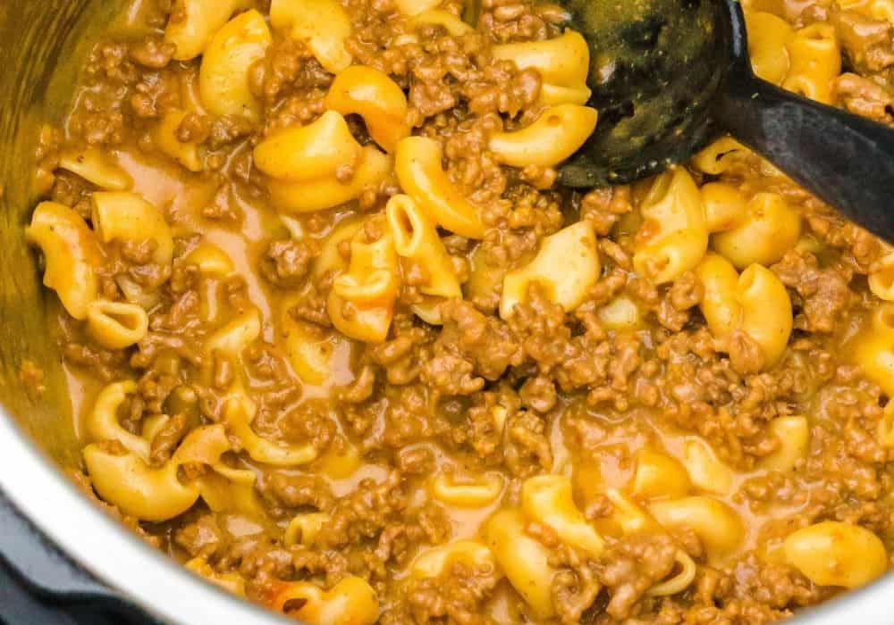 close-up overhead view of freshly cooked Hamburger Helper in the Instant Pot, featuring macaroni, ground beef, and a cheesy sauce, ready to be served with a black serving spoon.