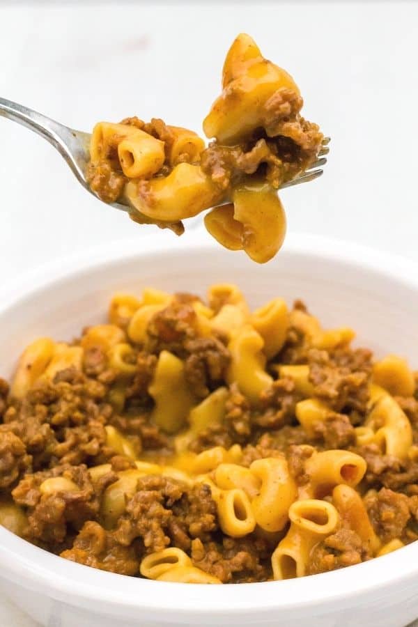 a fork lifting a bite of Instant Pot Hamburger Helper out of a white bowl