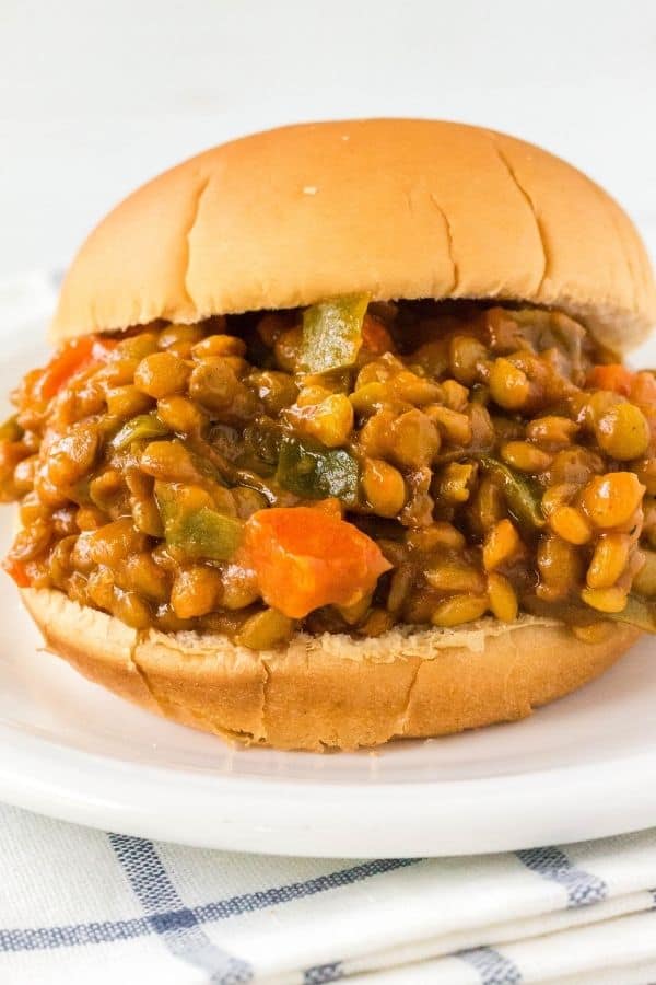 Sandwich bun stuffed with Instant Pot lentil sloppy joe filling, including lentils, onions, peppers, and carrots in a savory sauce.