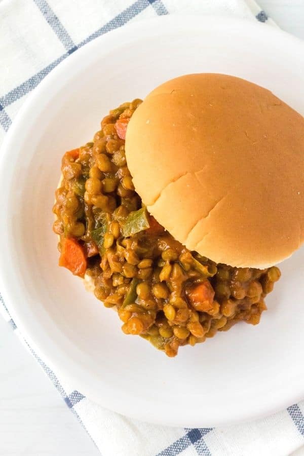 overhead view of an Instant Pot sloppy joe sandwich made with lentils instead of beef, served on a white plate atop a blue and white napkin