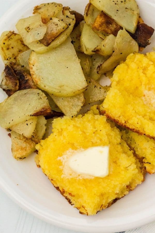 close-up view of a slice of cornbread with a pat of butter on it and a side of fried potatoes, which is what is traditionally served alongside old-fashioned pinto beans in West Virginia.