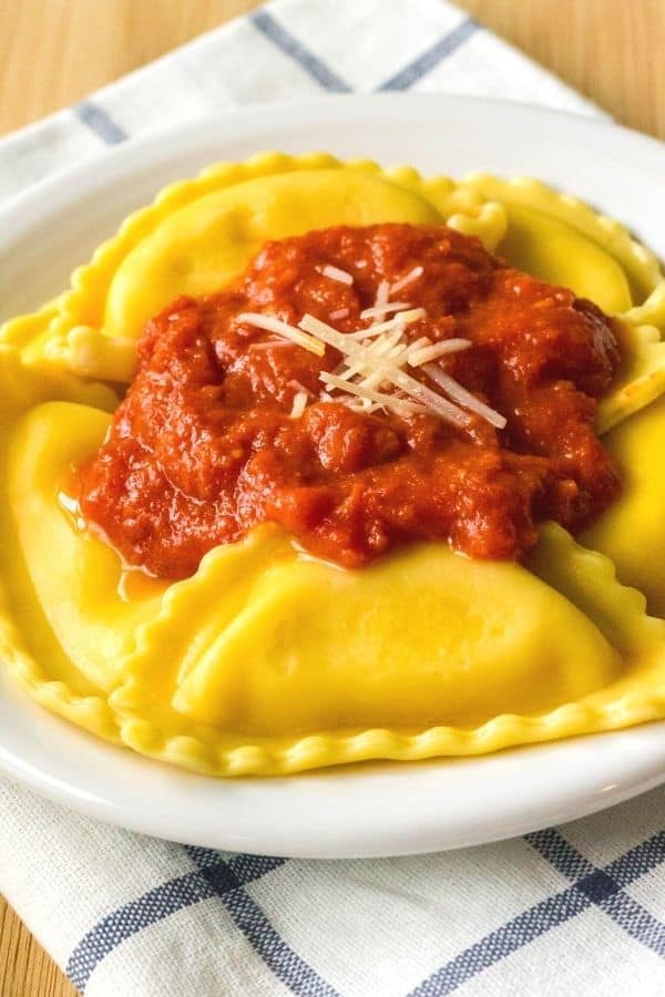 close-up side view of pressure cooker cheese tortellini topped with marinara sauce, served on a white plate