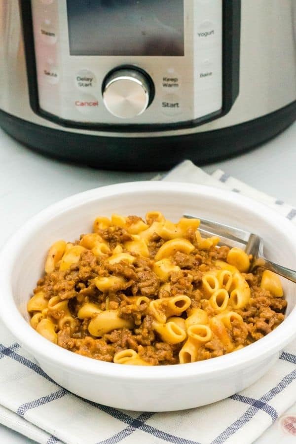 White bowl of Instant Pot Hamburger Helper on a blue and white towel in the foreground, with the Instant Pot pressure cooker in the background.