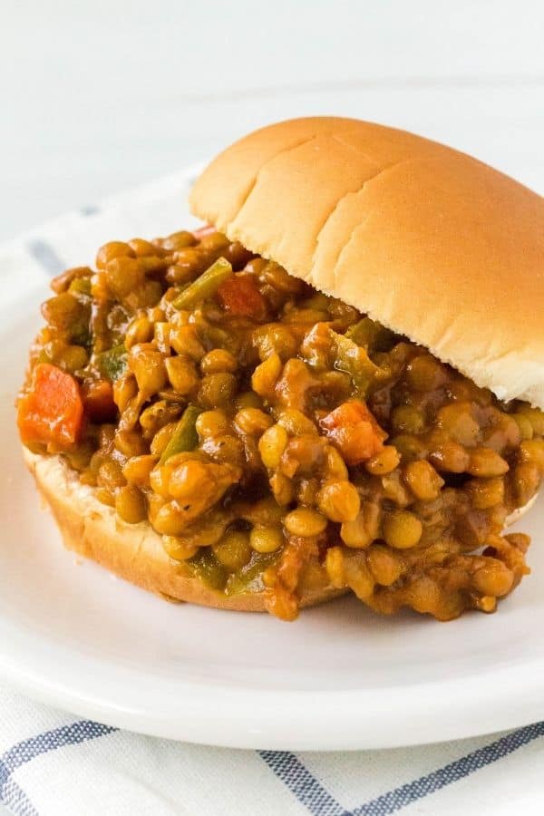 Side view of an Instant Pot lentil sloppy joe sandwich, with filling spilling off the bottom bun and the top bun offset to the side. Filling shows lentils, carrots, peppers, and sauce.