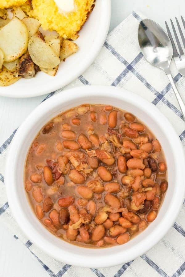 white bowl filled with Instant Pot Appalachian soup beans, served alongside a small white plate of fried potatoes and cornbread.