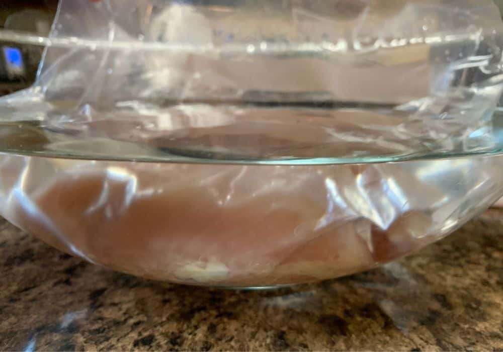 a chicken breast in a zip-top bag, using the displacement method to remove air from the bag by lowering the bag into water.