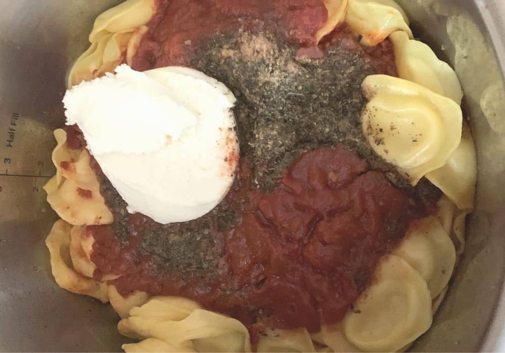 Freshly cooked frozen ravioli with meat sauce, along with a dollop of ricotta cheese to be mixed in to make lasagna casserole in the Instant Pot